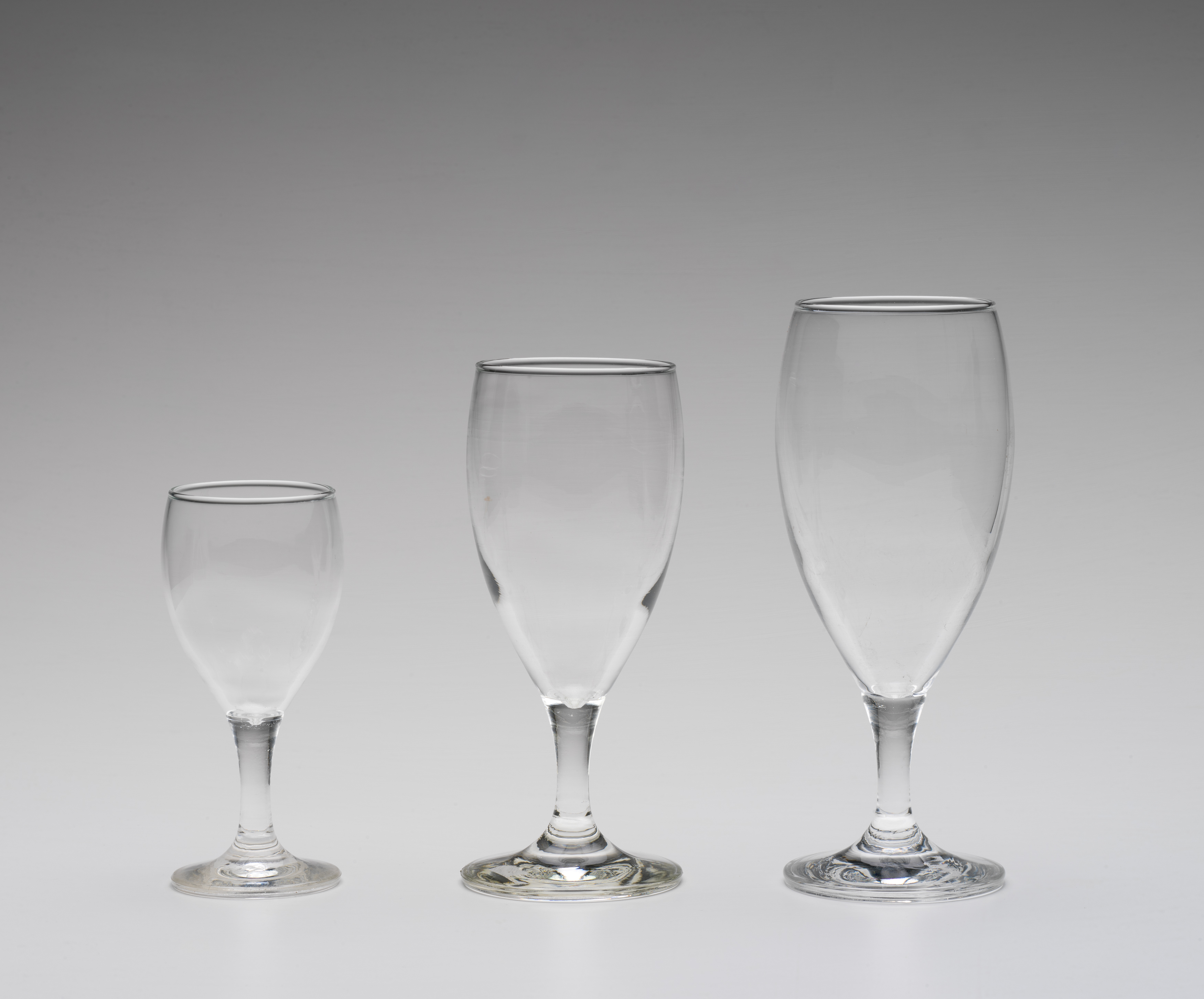 Three wine glasses of different sizes on a grey background.